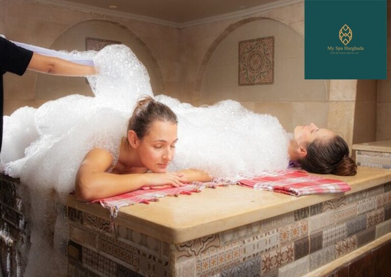 Two women relaxing on a heated marble platform covered in soap foam during The Complete Guide to the Turkish Hamam Experience.